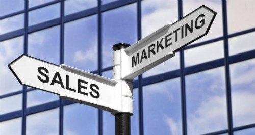 Concept image of Sales & Marketing on a signpost against a modern glass office building.