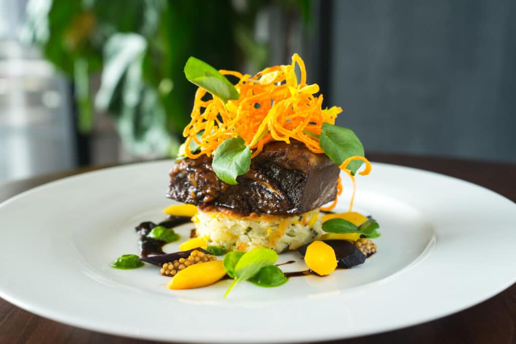 Copy of BRAISED BEEF SHORT RIB 2 Grilled corn scallion cake, tri-colored carrots, spinach silk, mustard seed caviar, organic watercress, yellow pea tendrils, crispy carrot nest and shitake demi (1)